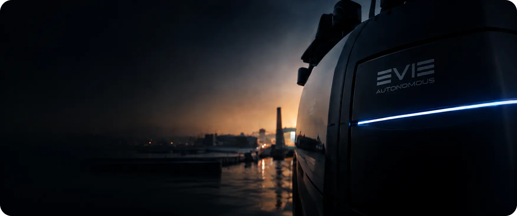 An EVIE Autonomous vehicle at dusk, dockside against a low sun